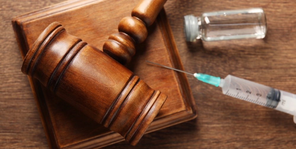 Gavel, syringe and glass vial on wooden table