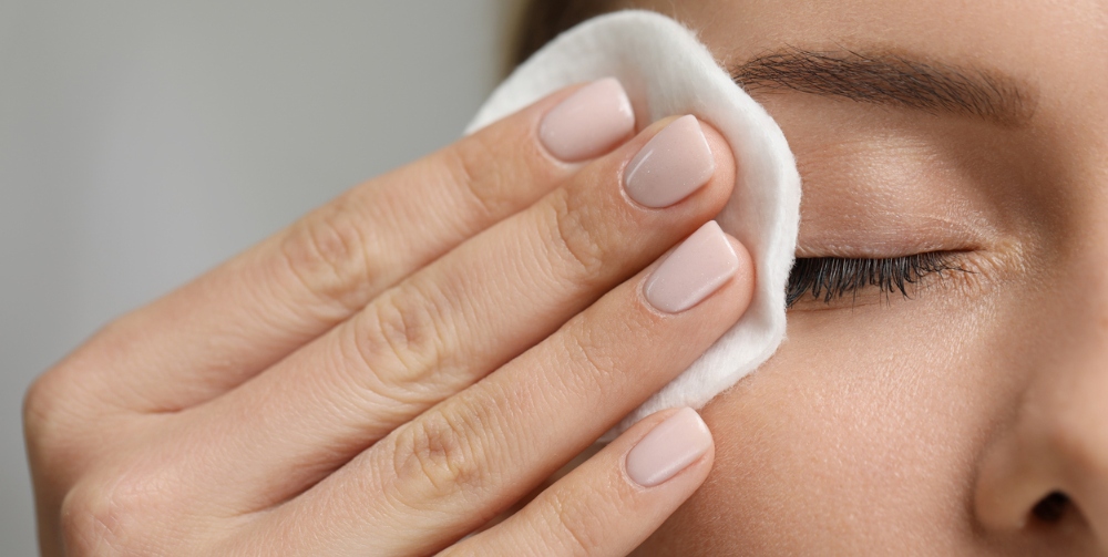 Woman removing makeup with cotton pad on grey background, closeup