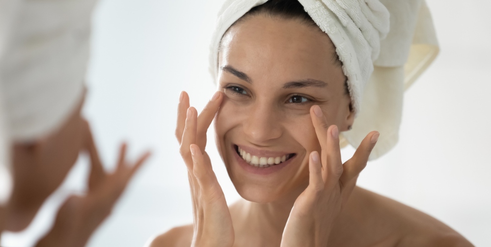 Smiling woman in towel on head after shower do facial procedures